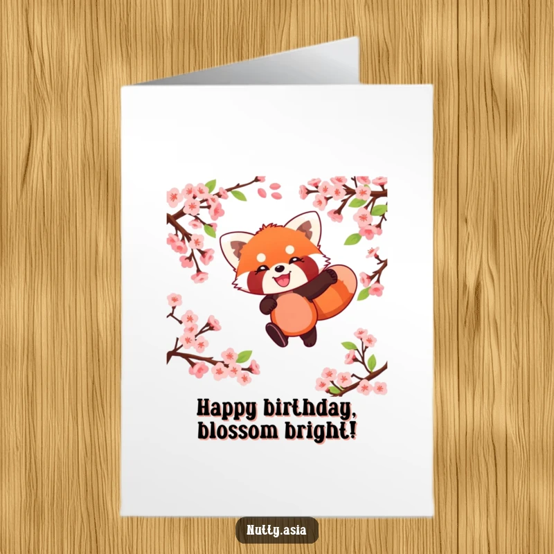 Funny free printable birthday card featuring a playful red panda leaping joyfully through pink cherry blossoms with a huge smile.